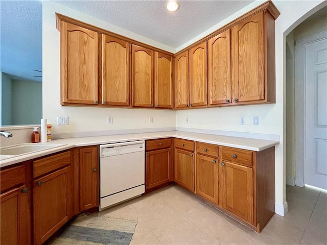 kitchen with white dishwasher, sink, light tile patterned floors, and a textured ceiling