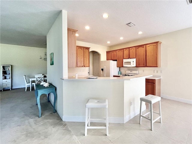 kitchen featuring a kitchen bar, white appliances, kitchen peninsula, and light tile patterned floors