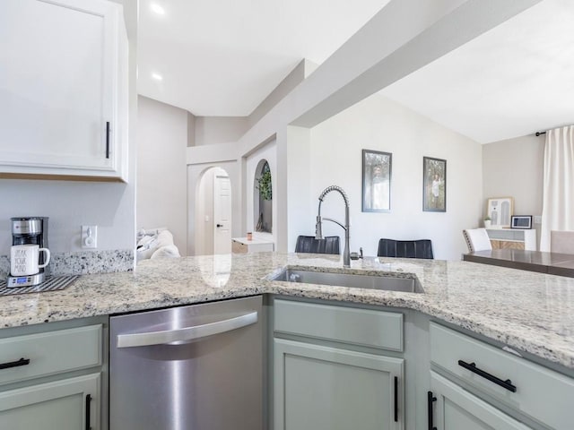 kitchen featuring arched walkways, dishwasher, light stone counters, and a sink