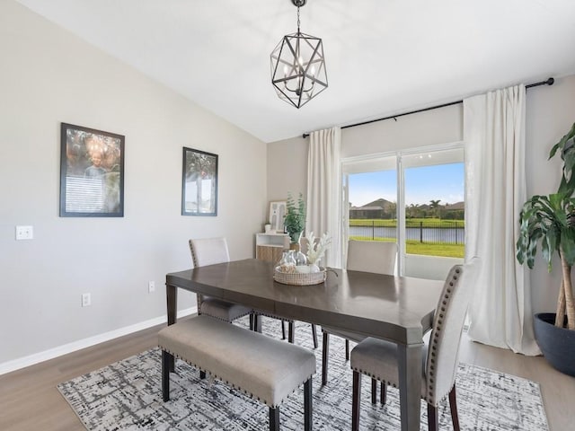 dining room featuring a notable chandelier, wood finished floors, baseboards, and vaulted ceiling