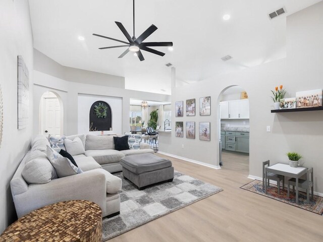 living area with visible vents, baseboards, light wood-type flooring, ceiling fan with notable chandelier, and arched walkways