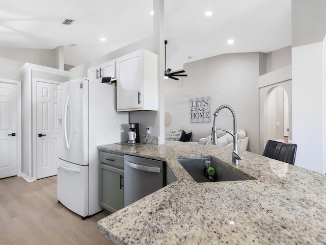 kitchen with light stone countertops, arched walkways, a sink, vaulted ceiling, and stainless steel dishwasher