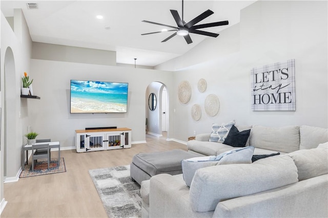 living area featuring visible vents, a ceiling fan, arched walkways, light wood finished floors, and baseboards