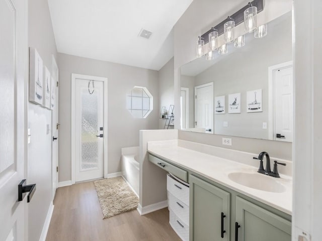 bathroom featuring visible vents, baseboards, wood finished floors, a bath, and vanity