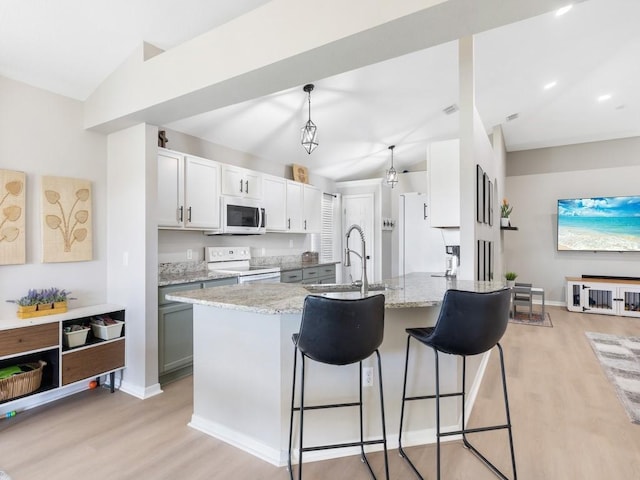 kitchen with white appliances, light stone countertops, light wood finished floors, a breakfast bar, and a sink