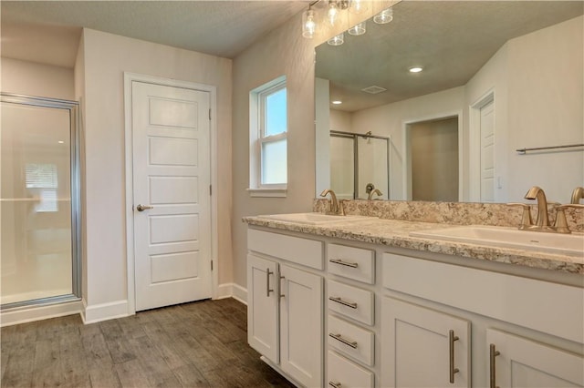 full bathroom with double vanity, a sink, a shower stall, and wood finished floors