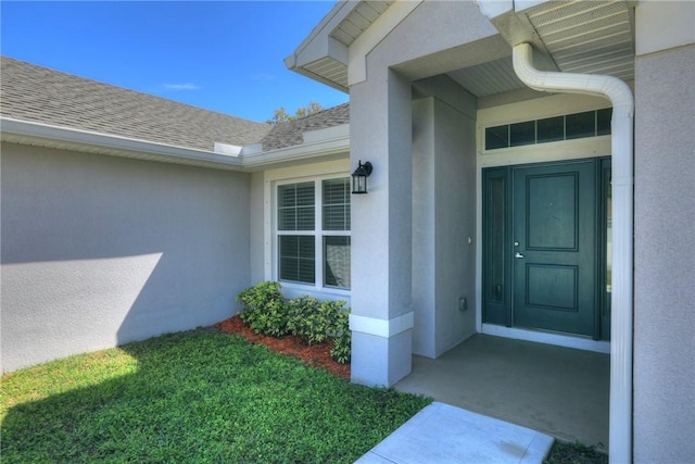 view of exterior entry with roof with shingles and stucco siding