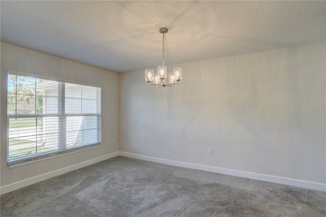 carpeted empty room featuring a chandelier, a textured ceiling, and baseboards