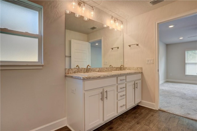 full bath with double vanity, baseboards, visible vents, wood finished floors, and a sink