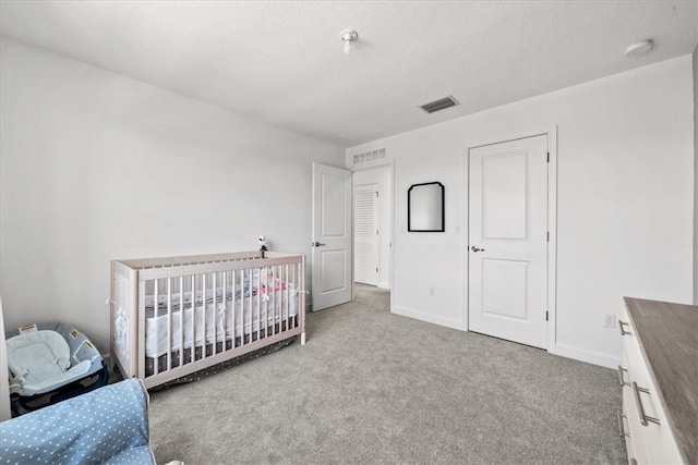 bedroom with a textured ceiling, light colored carpet, and a crib