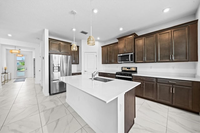 kitchen featuring stainless steel appliances, a center island with sink, dark brown cabinetry, sink, and decorative light fixtures