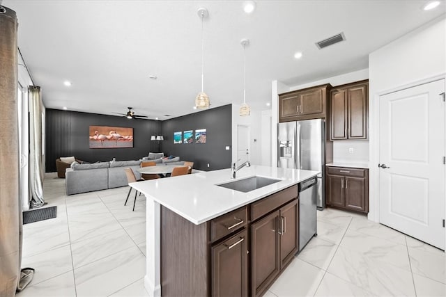 kitchen featuring sink, appliances with stainless steel finishes, ceiling fan, decorative light fixtures, and an island with sink