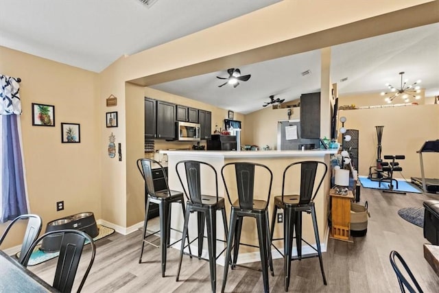 kitchen with a breakfast bar, light hardwood / wood-style floors, ceiling fan with notable chandelier, vaulted ceiling, and kitchen peninsula