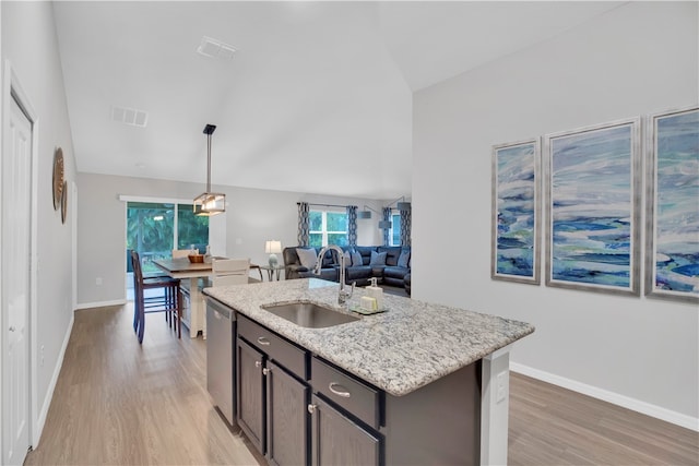 kitchen with sink, light stone countertops, hanging light fixtures, a kitchen island with sink, and light hardwood / wood-style flooring