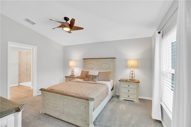 bedroom with vaulted ceiling, light colored carpet, ceiling fan, and ensuite bathroom