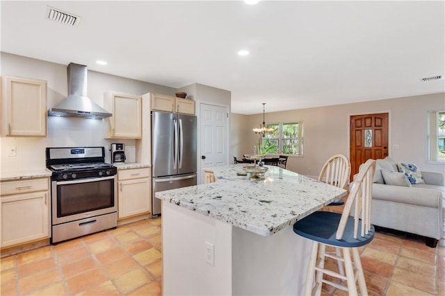 kitchen featuring wall chimney exhaust hood, a breakfast bar, a kitchen island, pendant lighting, and stainless steel appliances