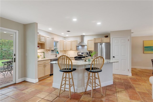 kitchen with a breakfast bar area, light stone counters, appliances with stainless steel finishes, a kitchen island, and wall chimney range hood