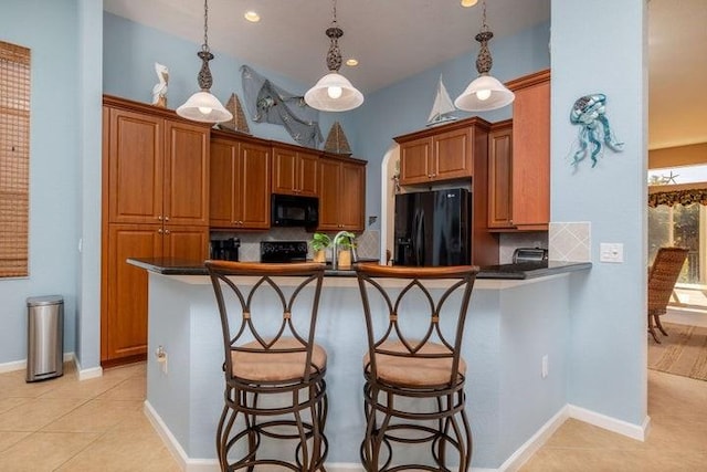 kitchen featuring kitchen peninsula, decorative backsplash, a breakfast bar, black appliances, and pendant lighting