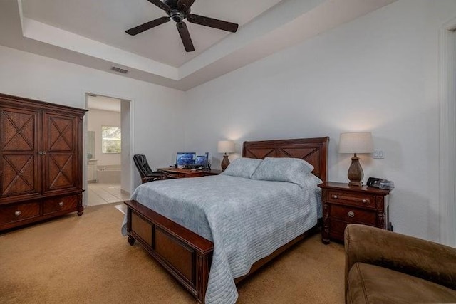 bedroom with a raised ceiling, ensuite bath, ceiling fan, and light carpet