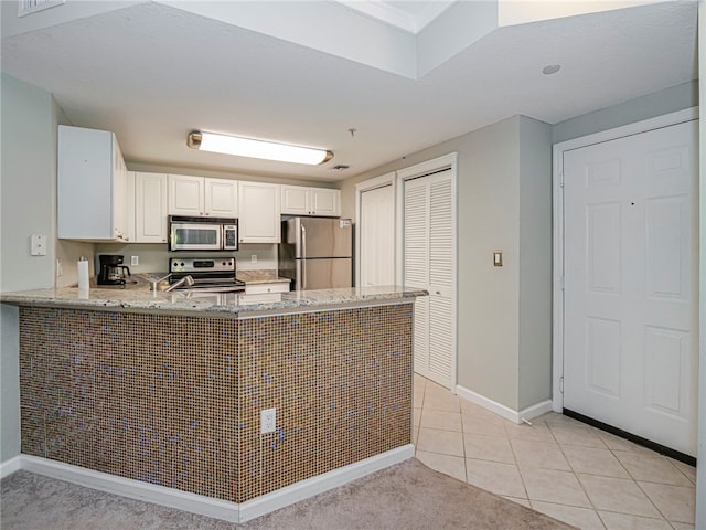 kitchen with stainless steel appliances, light stone counters, white cabinets, kitchen peninsula, and light tile patterned floors