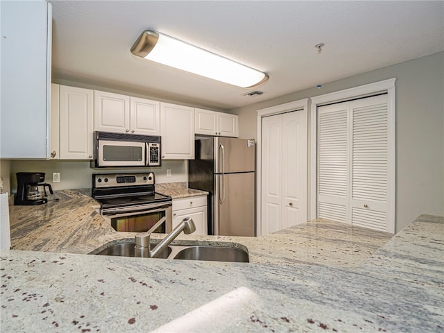 kitchen with appliances with stainless steel finishes, sink, light stone counters, and white cabinets