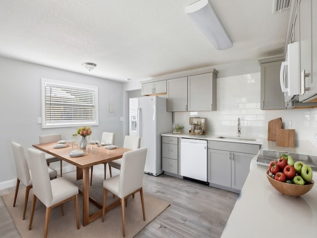 kitchen with light hardwood / wood-style floors, sink, a textured ceiling, white appliances, and gray cabinetry