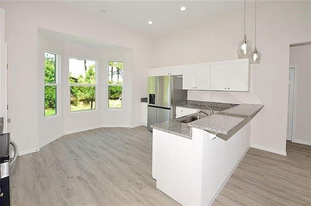 kitchen with stone countertops, stainless steel fridge, kitchen peninsula, pendant lighting, and white cabinets