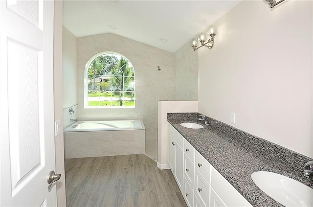 bathroom with hardwood / wood-style floors, vanity, vaulted ceiling, and a relaxing tiled tub