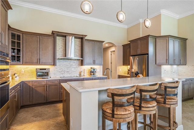 kitchen with a center island with sink, a breakfast bar area, wall chimney exhaust hood, and appliances with stainless steel finishes