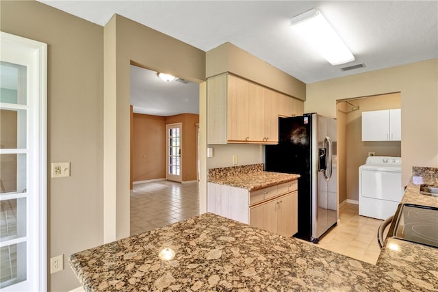 kitchen featuring light brown cabinetry, stainless steel fridge with ice dispenser, black range, and washer / dryer