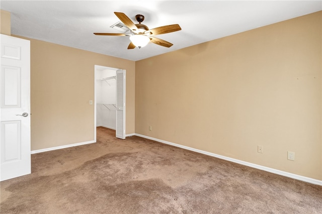 unfurnished bedroom with ceiling fan, a closet, a walk in closet, and carpet