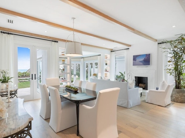 dining room with a brick fireplace, light hardwood / wood-style flooring, beam ceiling, and french doors