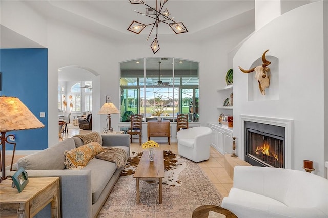 living area with a warm lit fireplace, a high ceiling, arched walkways, and light tile patterned flooring