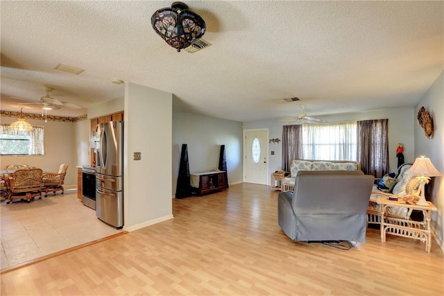 living room featuring ceiling fan, a textured ceiling, and light wood-type flooring