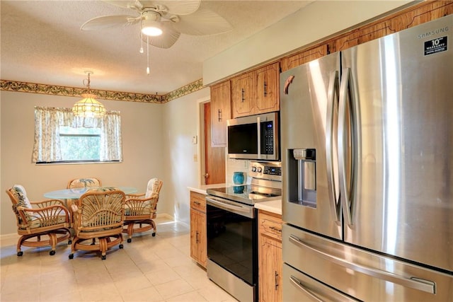 kitchen featuring hanging light fixtures, light tile patterned floors, ceiling fan, stainless steel appliances, and a textured ceiling