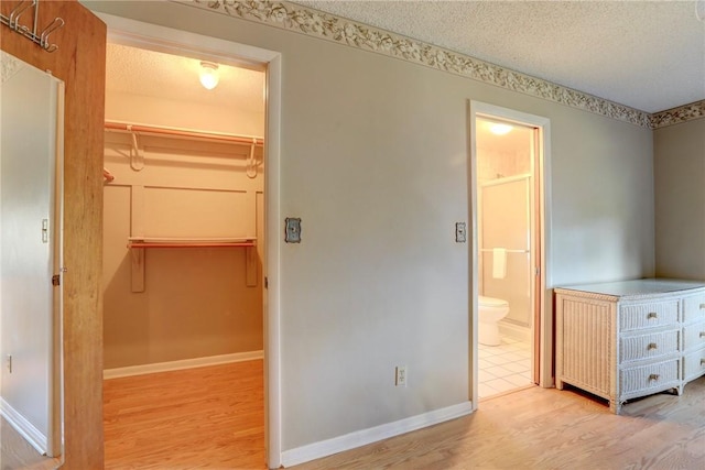 unfurnished bedroom featuring a spacious closet, a textured ceiling, and light wood-type flooring