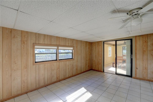 spare room with a drop ceiling, light tile patterned floors, ceiling fan, and wood walls