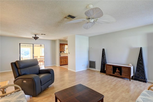 living room featuring ceiling fan, a textured ceiling, and light wood-type flooring