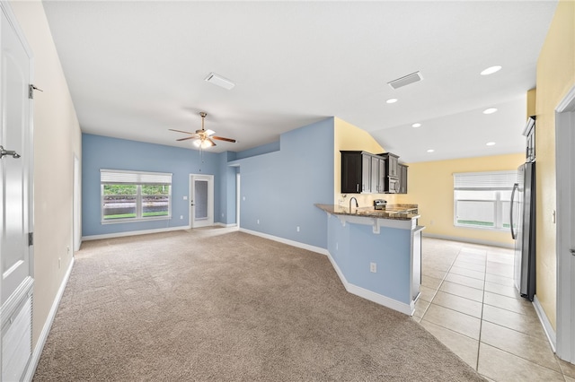 kitchen with stainless steel refrigerator, a kitchen bar, kitchen peninsula, light colored carpet, and ceiling fan