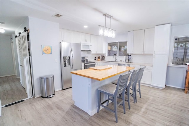 kitchen featuring a center island, a barn door, light wood-type flooring, white cabinetry, and stainless steel appliances