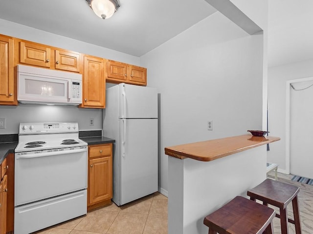 kitchen with a kitchen bar, light tile patterned floors, and white appliances