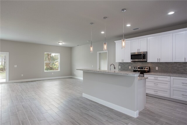 kitchen featuring a center island with sink, white cabinetry, appliances with stainless steel finishes, decorative light fixtures, and light wood-type flooring