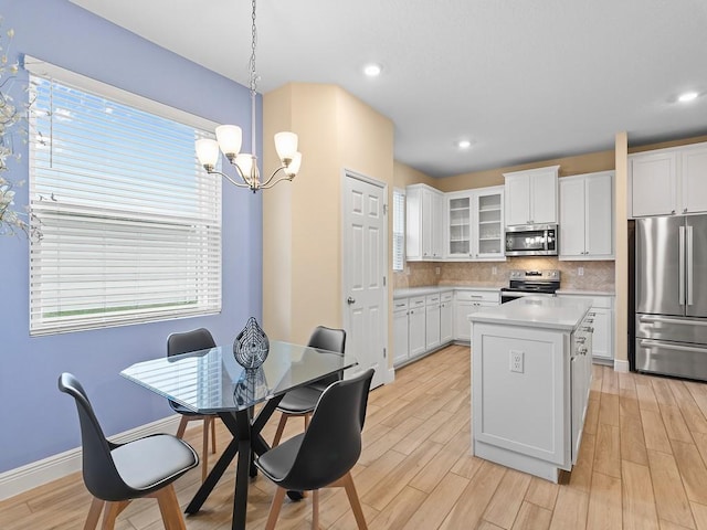 kitchen featuring stainless steel appliances, a center island, decorative backsplash, white cabinets, and decorative light fixtures