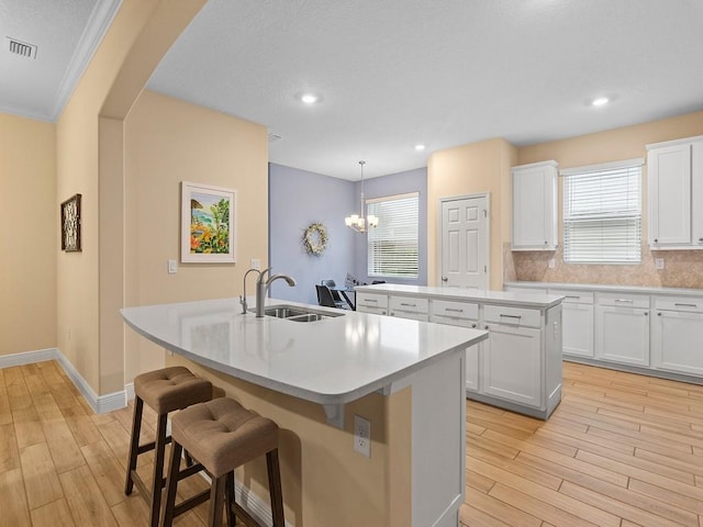 kitchen featuring sink, a center island with sink, pendant lighting, decorative backsplash, and white cabinets