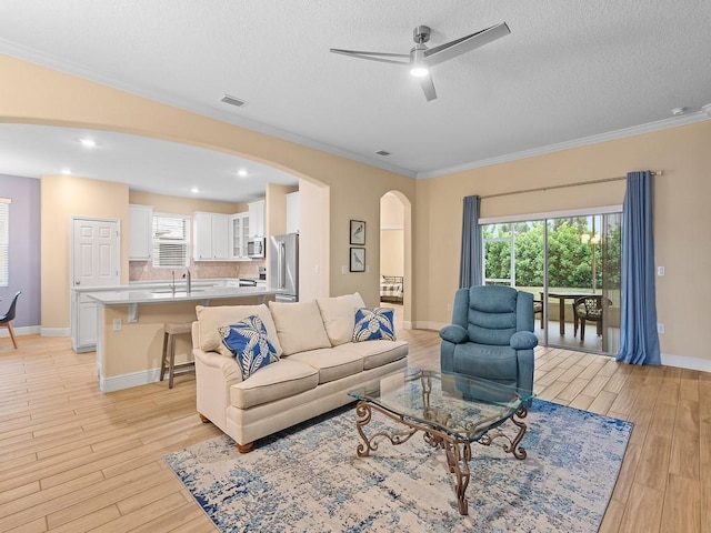 living room featuring crown molding, sink, ceiling fan, and light wood-type flooring