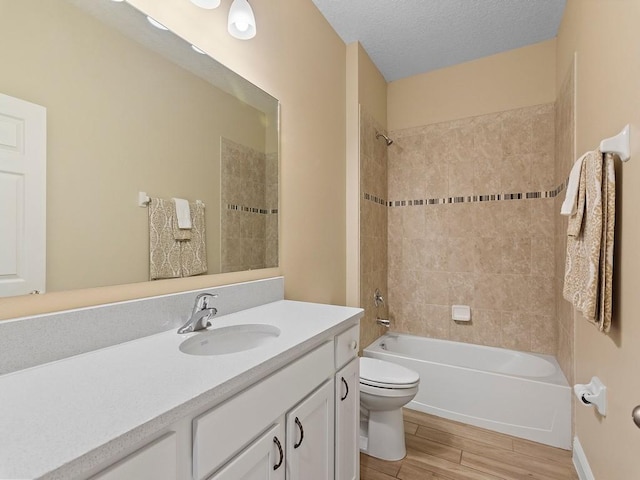 full bathroom with tiled shower / bath combo, vanity, a textured ceiling, and toilet