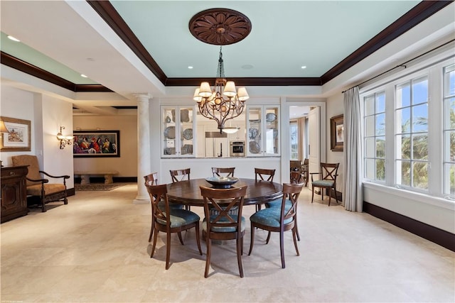 dining space featuring ornamental molding, a raised ceiling, a chandelier, and ornate columns