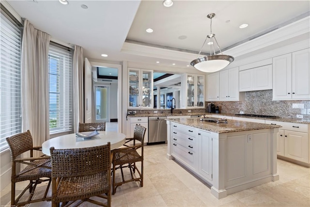 kitchen with sink, a tray ceiling, white cabinets, a kitchen island, and stainless steel dishwasher