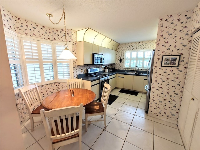 kitchen featuring cream cabinets, appliances with stainless steel finishes, light tile patterned floors, sink, and decorative light fixtures