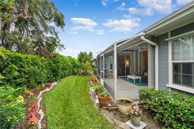 view of yard featuring a patio area, ceiling fan, and glass enclosure